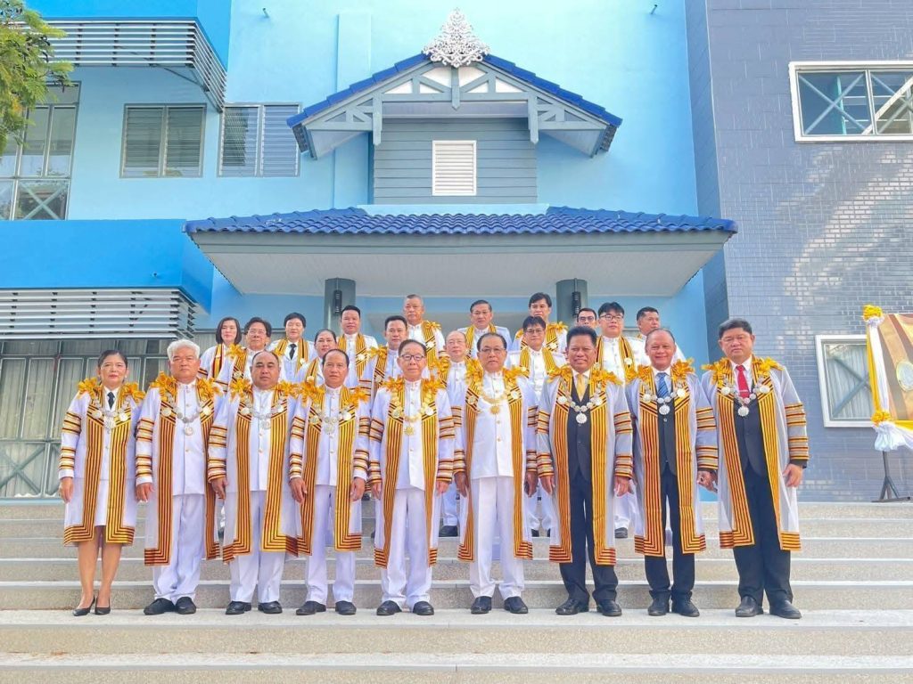 คณะผู้ทรงคุณวุฒิบัณฑิตกิตติมศักดิ์ ถ่ายภาพร่วมกันบริเวณด้านหน้าตึกสีฟ้าอ่อนของสถานศึกษา แสดงถึงบรรยากาศของความภาคภูมิใจ