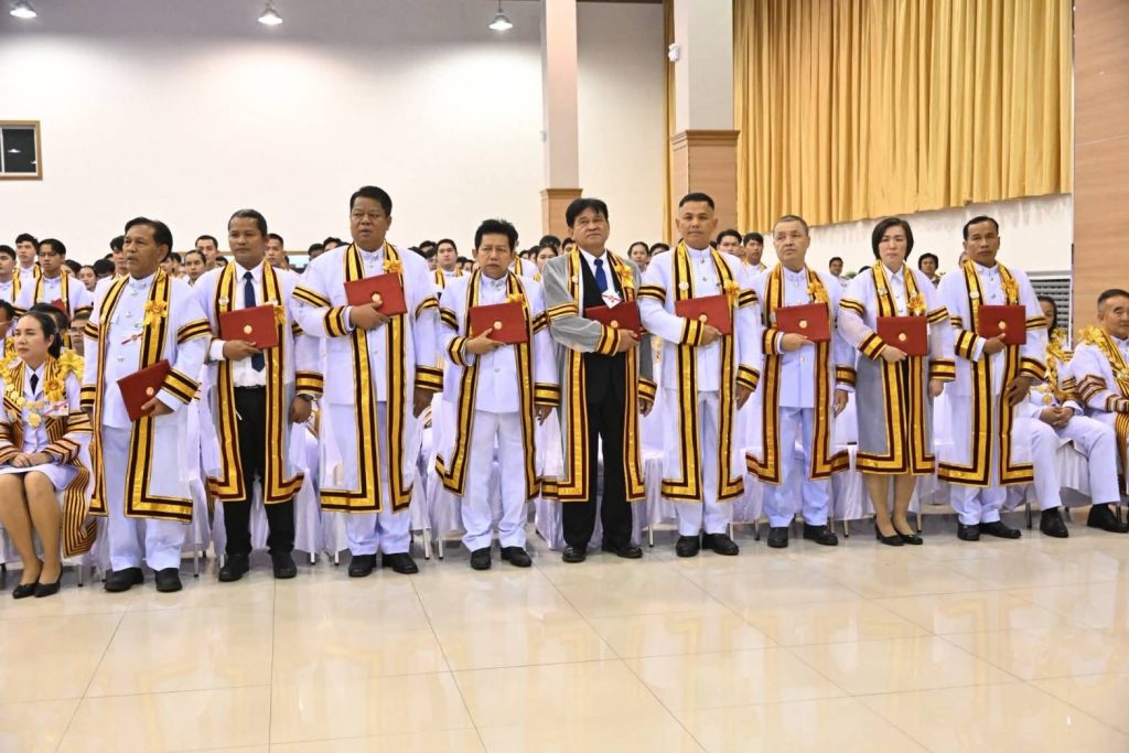 บัณฑิตกิตติมศักดิ์ทั้ง 11 ท่าน ยืนถือปริญญาบัตรสีแดง ขณะรอฟังประกาศรายชื่อภายในหอประชุม โดยมีคุณภัทรปภา คิรินทร์ อยู่ทางขวาในแถวหน้า